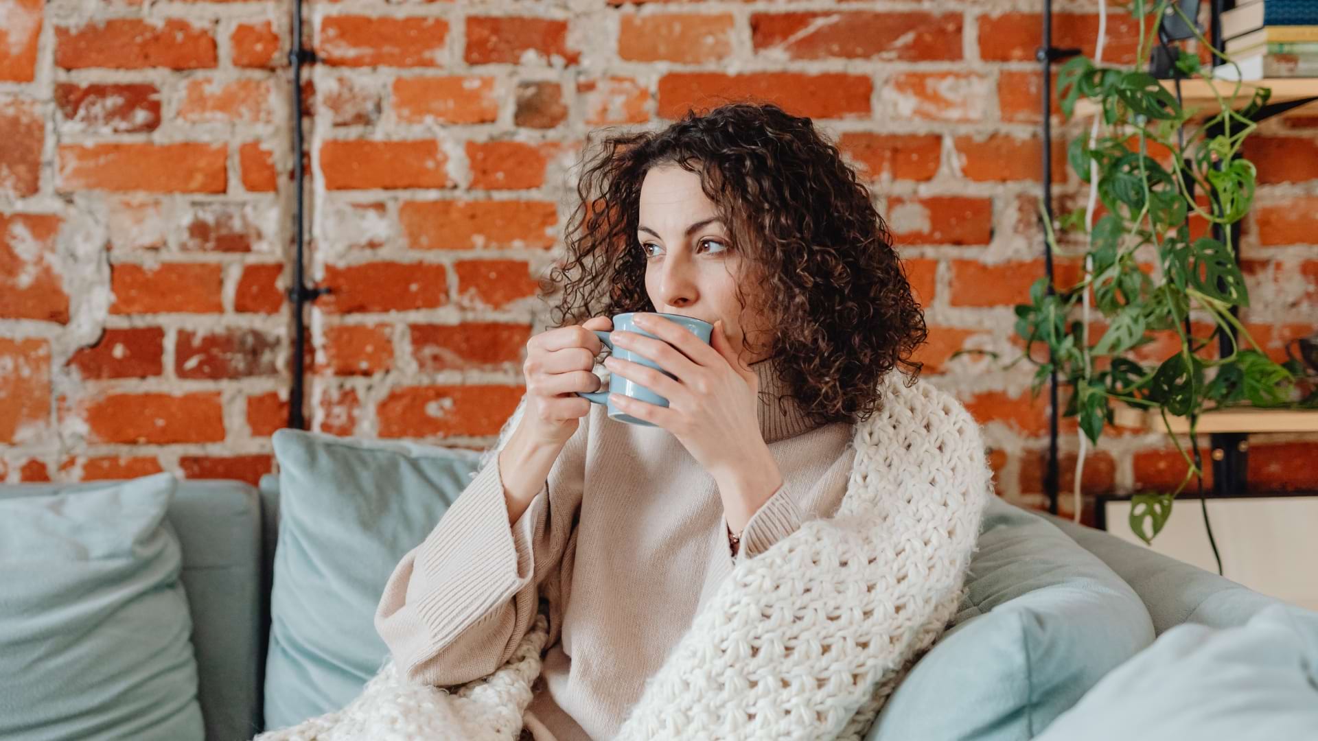 Personne assise confortablement sur un canapé, enveloppée dans une couverture et tenant une tasse dans un salon chaleureux.