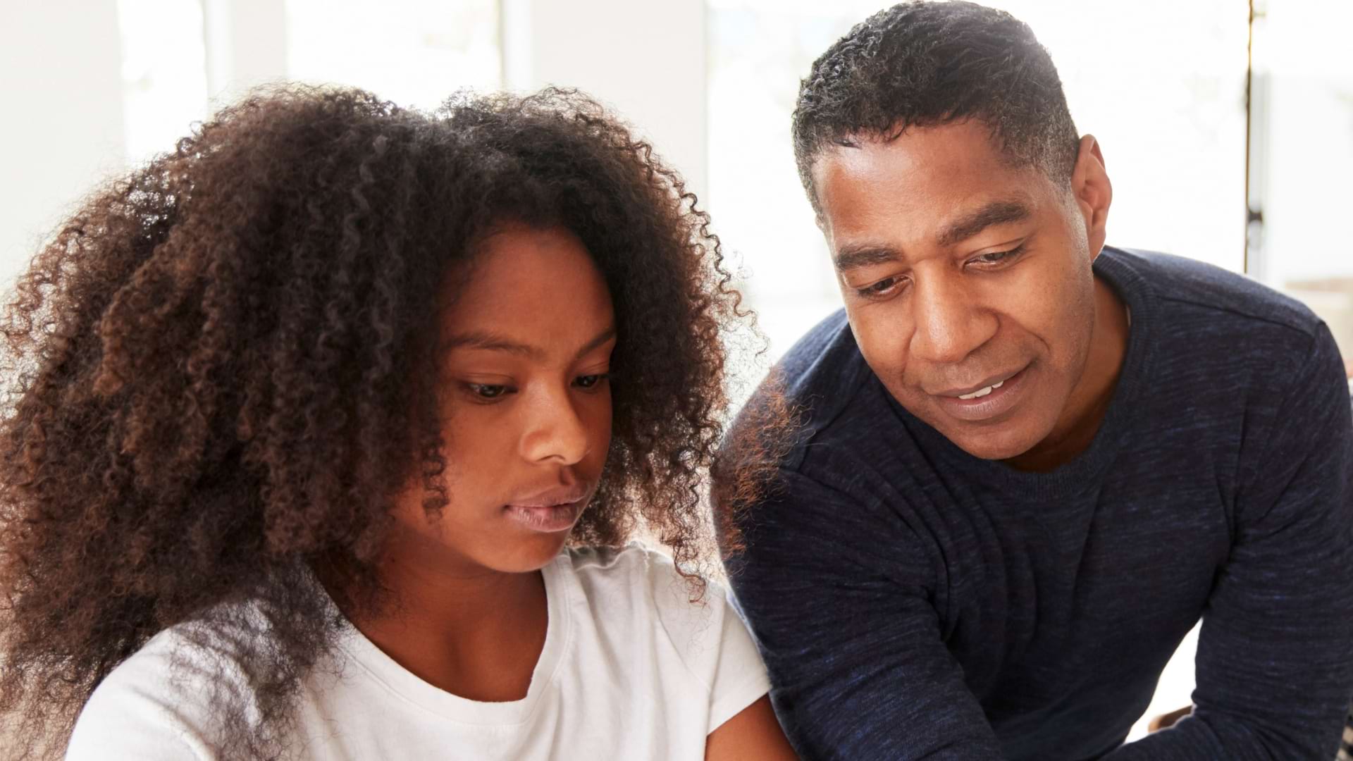 Personne aidant un enfant à réaliser une activité d’apprentissage à une table dans un environnement lumineux.